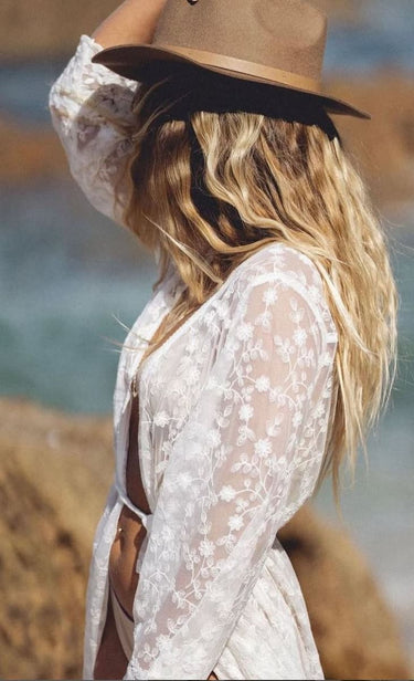 Woman wearing a lace top and wide-brimmed hat by a body of water